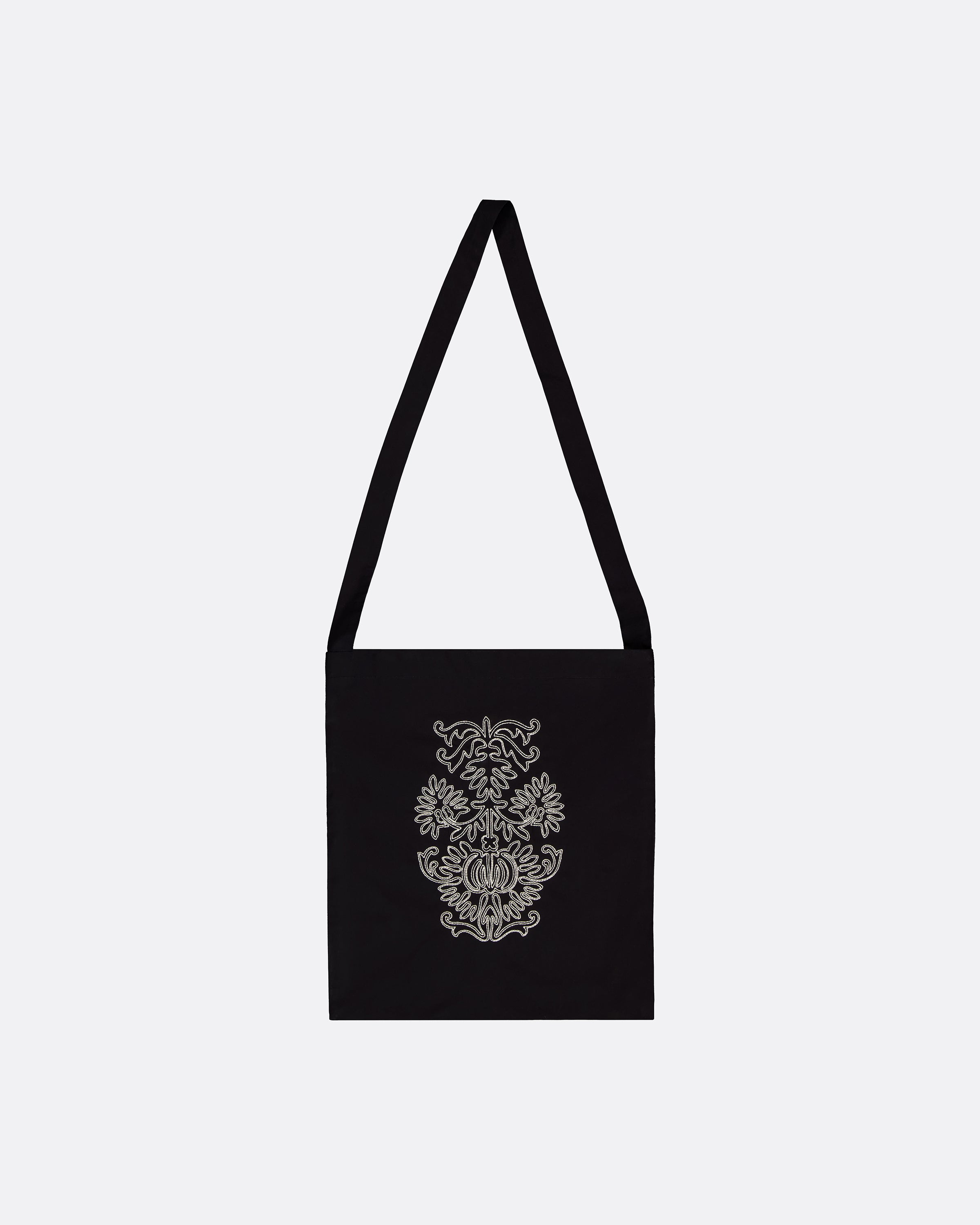 A black canvas shoulder bag with a long strap, featuring a white ornate damask-style pattern printed on the front, set against a plain light gray background.