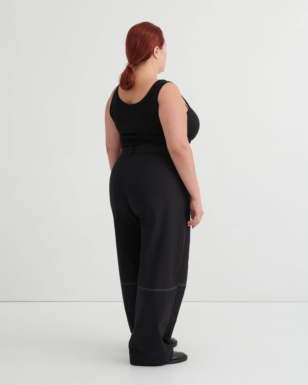 Person wearing a black singlet tucked into black pants against a white background