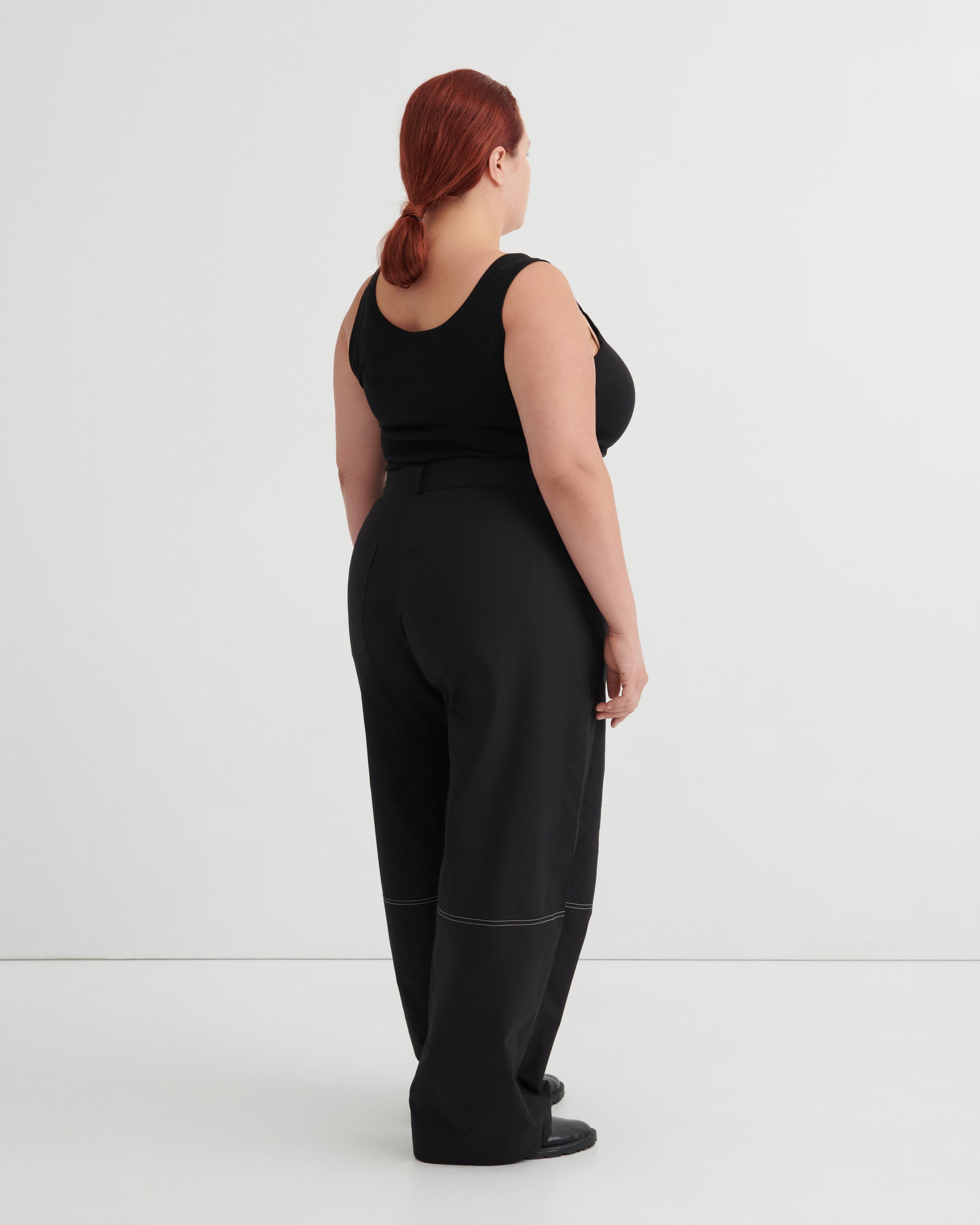 Person wearing a black singlet tucked into black pants against a white background