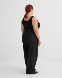 Person wearing a black singlet tucked into black pants against a white background