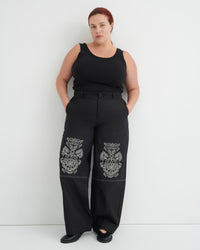 Person wearing black sleeveless top and pants with floral patterns on a white background