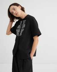 Person wearing a black outfit with white embroidery on a plain background