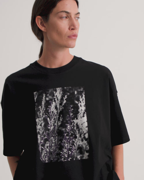 A model wearing an oversized black tee with a graphic floral placement print and black wide leg pants.