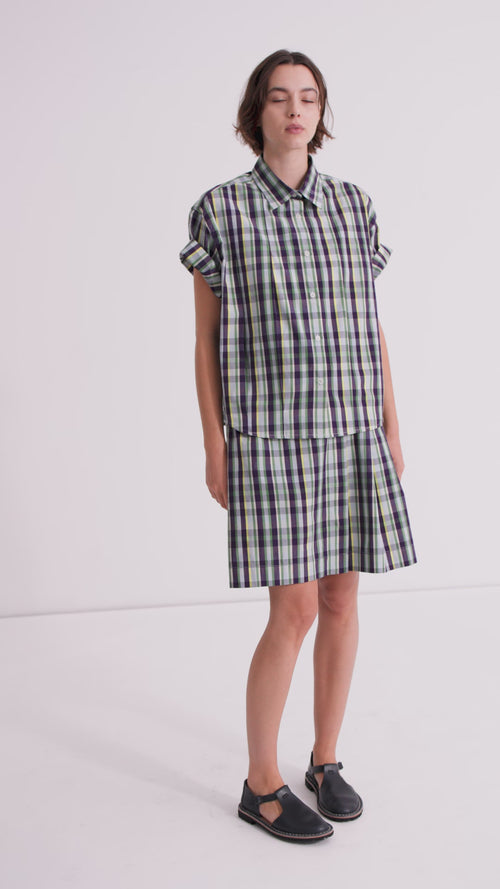A model wearing matching plaid shirt and short skirt with black mary janes.