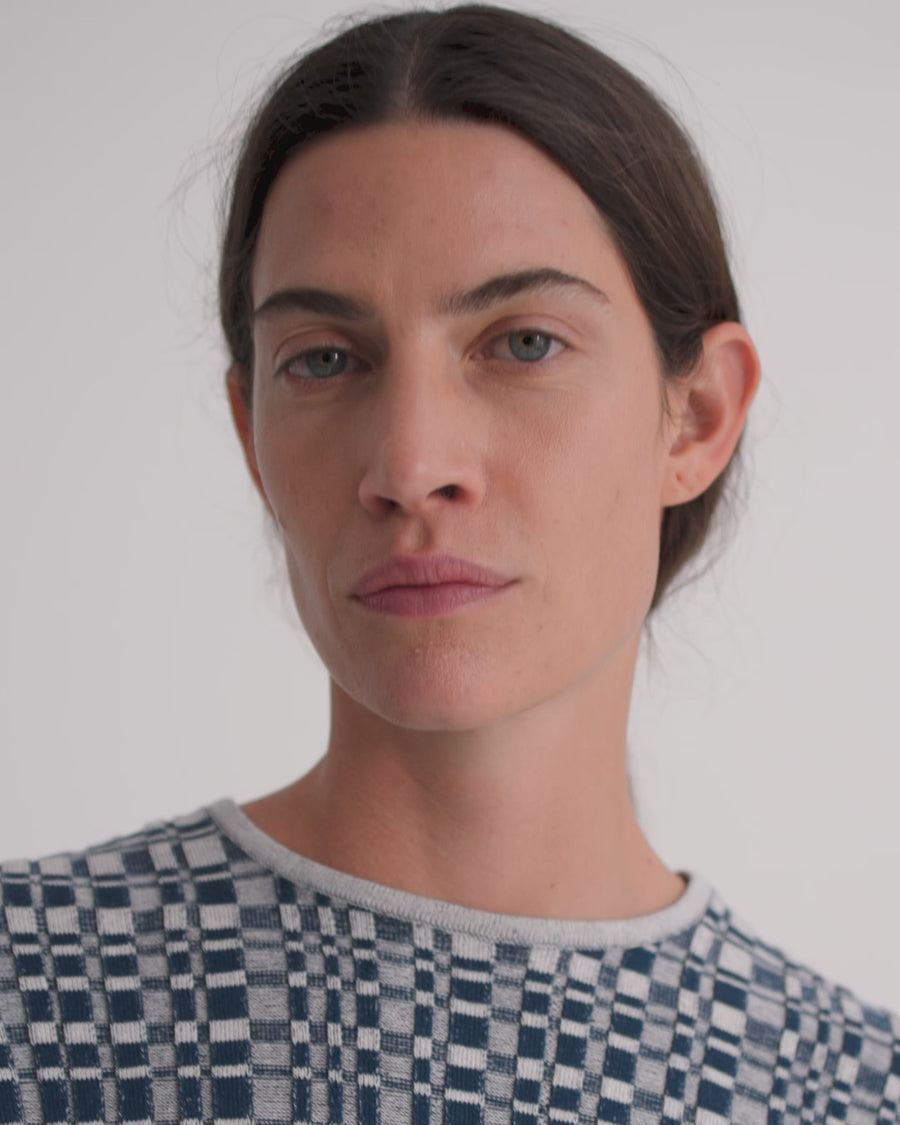 A women wearing a blue check knit top and dark denim shorts.