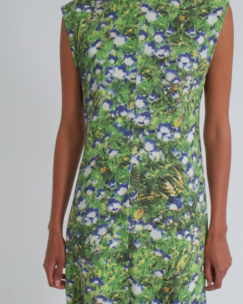 A women wearing a long sleeveless floral green dress against a grey backdrop.