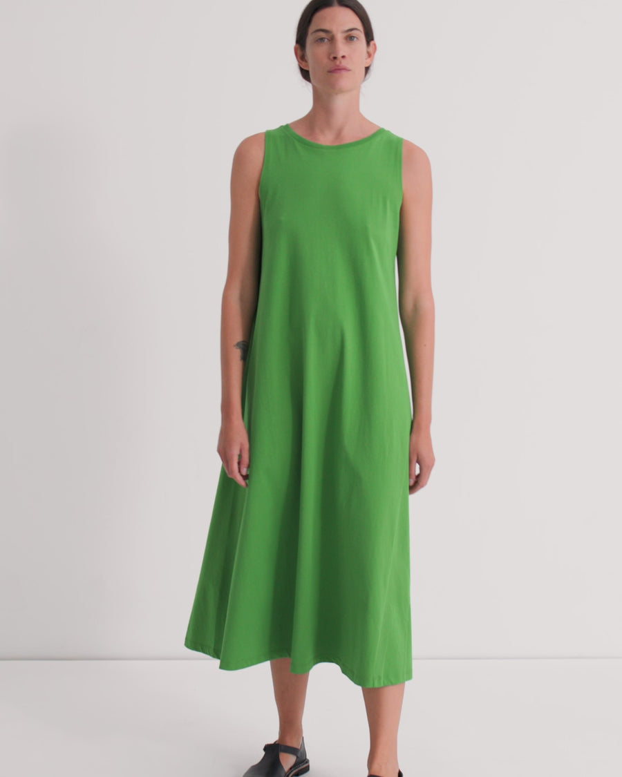 A women wearing a sleeveless green a-line dress standing against a light grey background.