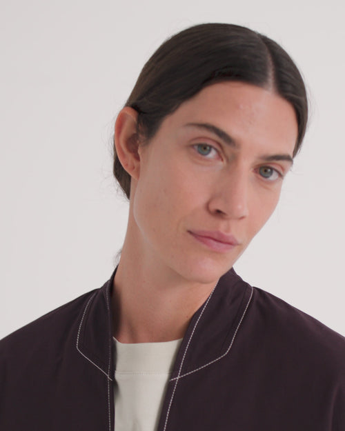 A video of a model wearing a dark brown collarless blazer over an off white shirt with matching dark brown pants.