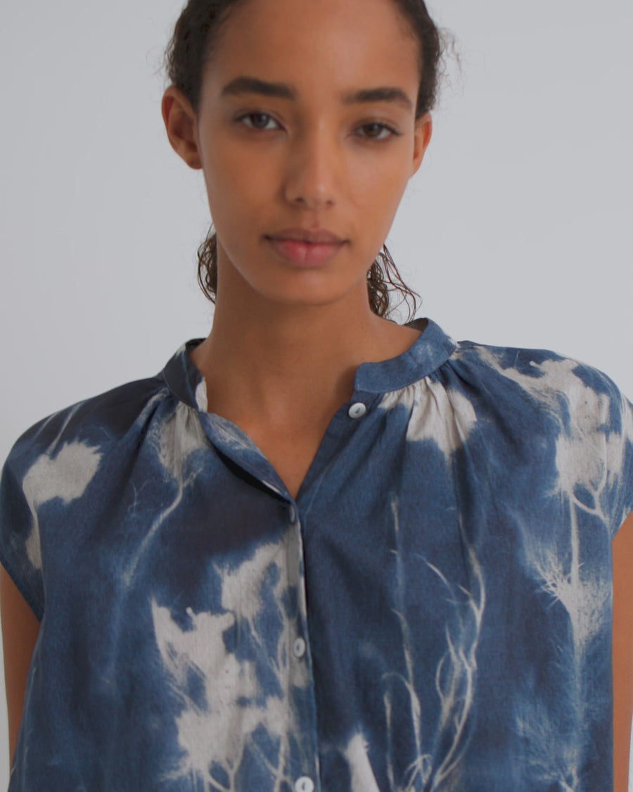 A women wearing a sleeveless blouse in a blue floral cyanotype print and dark denim shorts.