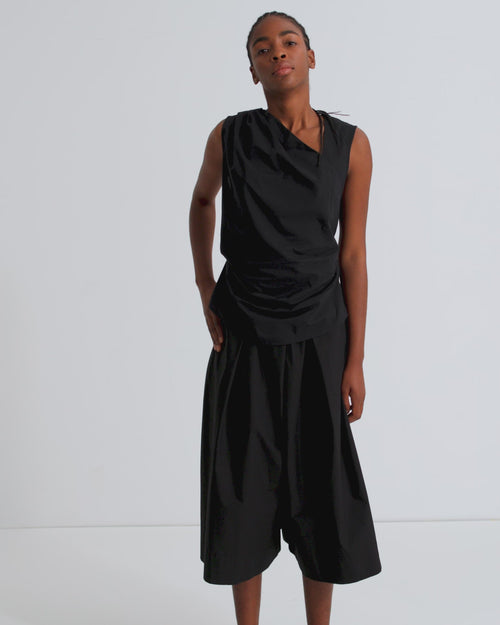 A women wearing an asymmetric black sleeveless top and wide leg pants.