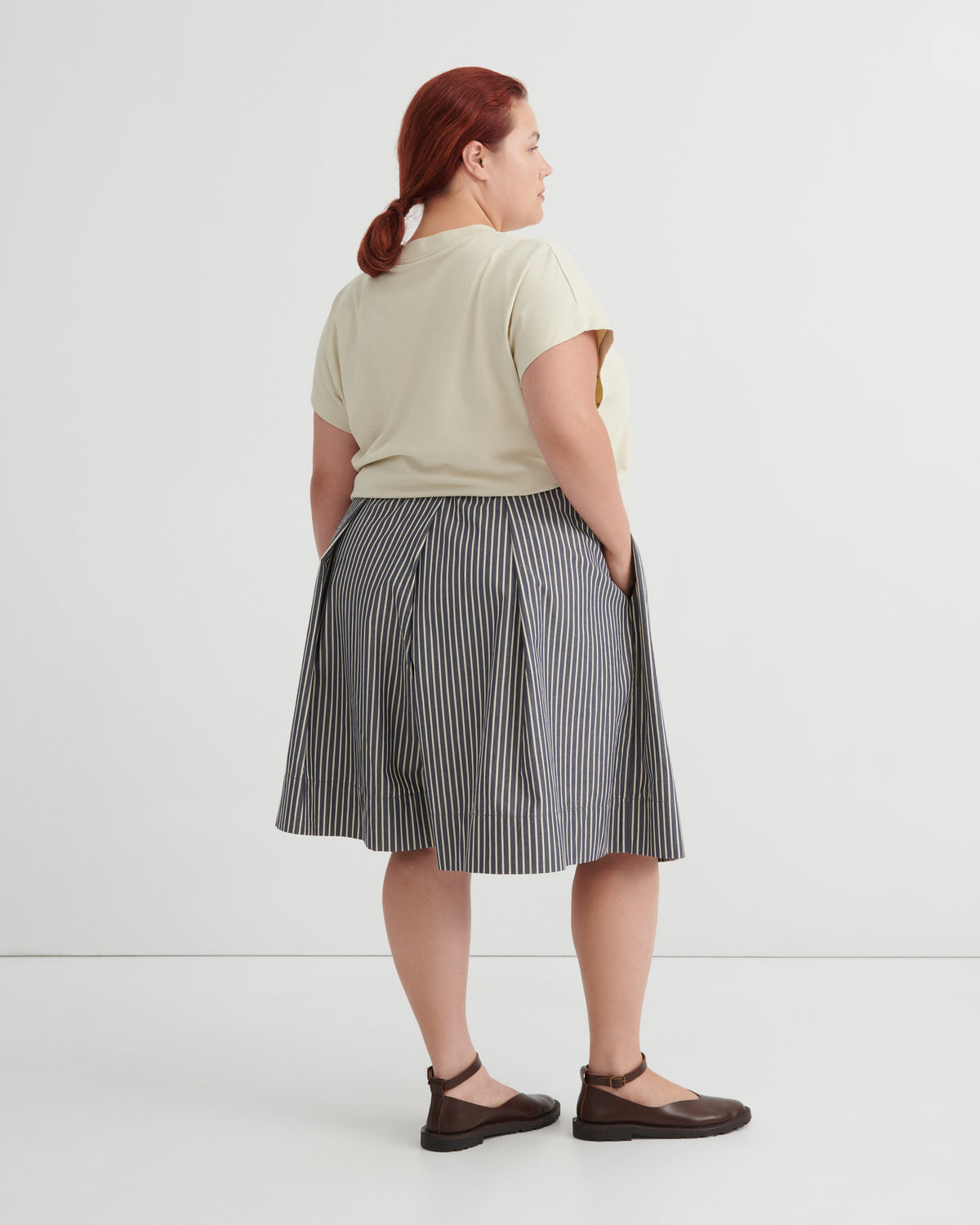 Person wearing a light green shirt and striped skirt on a white background