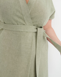 Close-up of a sage green wrap dress with a matching tie belt, featuring a textured linen-like fabric and subtle vertical stripe detailing.