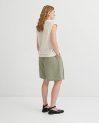 Woman wearing a beige sleeveless crochet top and green shorts on a white background