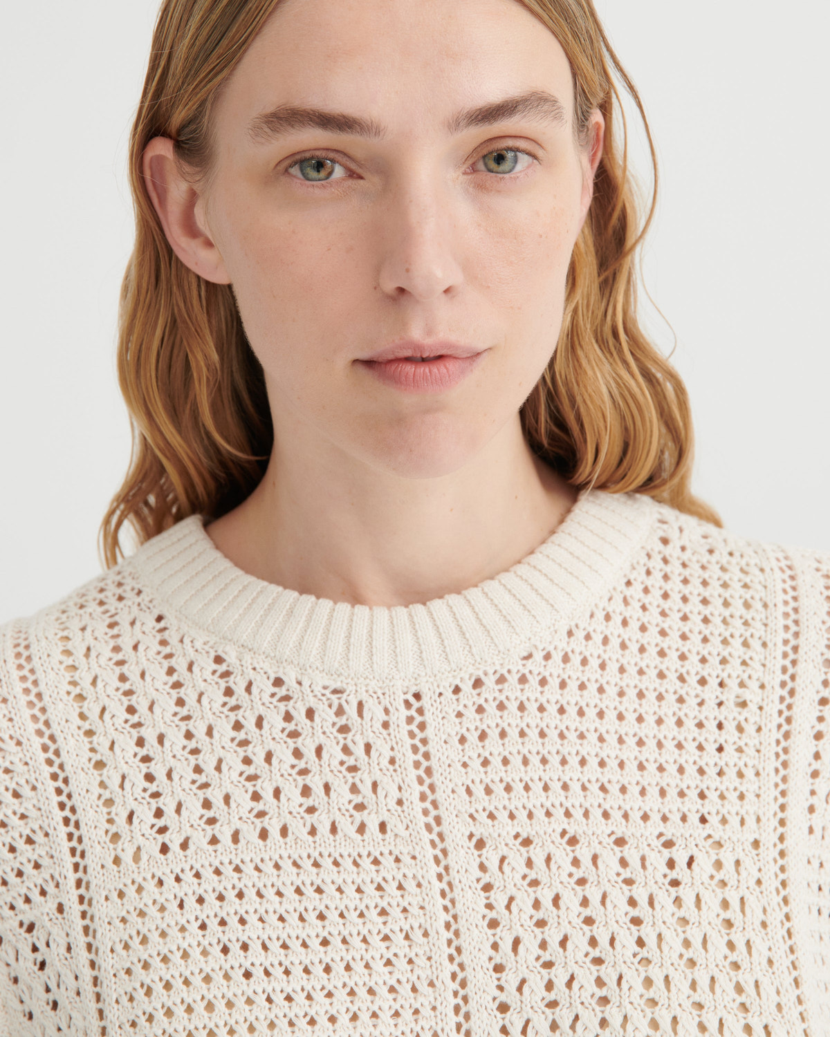 Person wearing a beige knit sweater on a white background