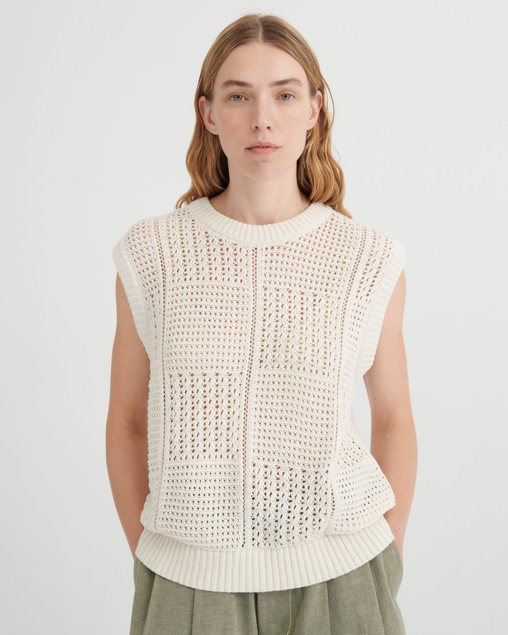Woman wearing a white sleeveless knitted top against a plain background
