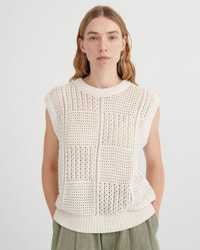 Woman wearing a white sleeveless knitted top against a plain background