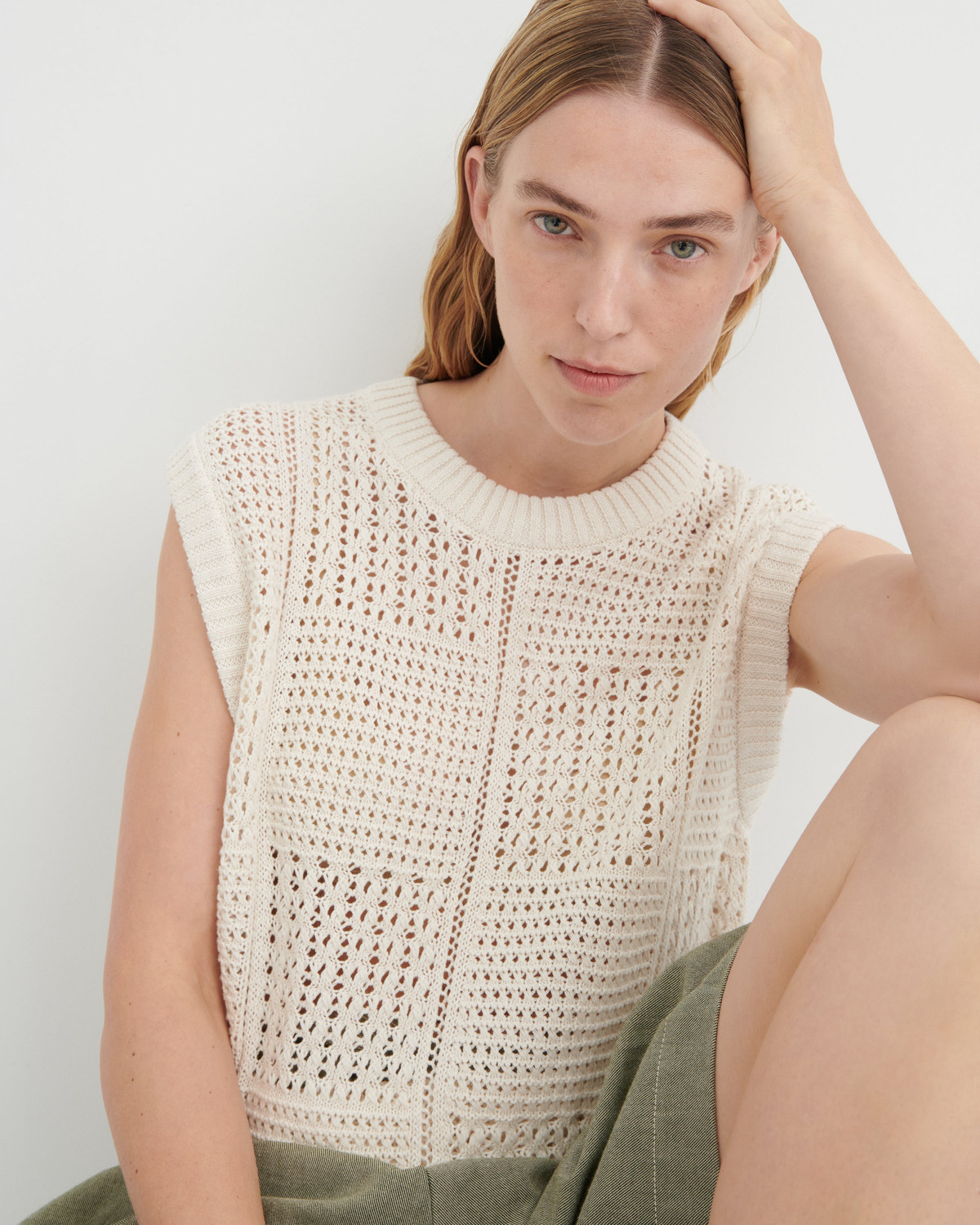 Woman wearing a beige sleeveless crochet top against a white background